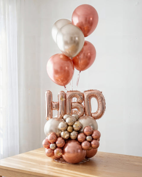 Columna de globos con helio "Golden Hour" para cumpleaños en oro rosa, champán y perla, con letras HBD y mariposas — Perú Balloons, Lima