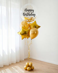 Bouquet de globos Happy Birthday dorado con burbuja transparente, confetti, estrellas metálicas y base decorativa