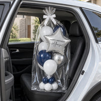 Bouquet de globos con estrella plateada, envuelto en celofán sobre el asiento trasero de un auto