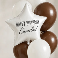 Globo de estrella blanco con la frase Happy Birthday Camila, en primer plano entre globos blancos y chocolate.
