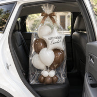Bouquet de globos con estrella, envuelto en celofán y con lazo café, en el asiento trasero de un auto.