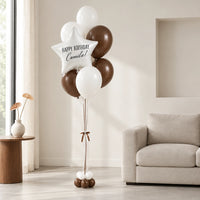 Bouquet de globos con estrella de cumpleaños junto a un sofá en una sala luminosa.