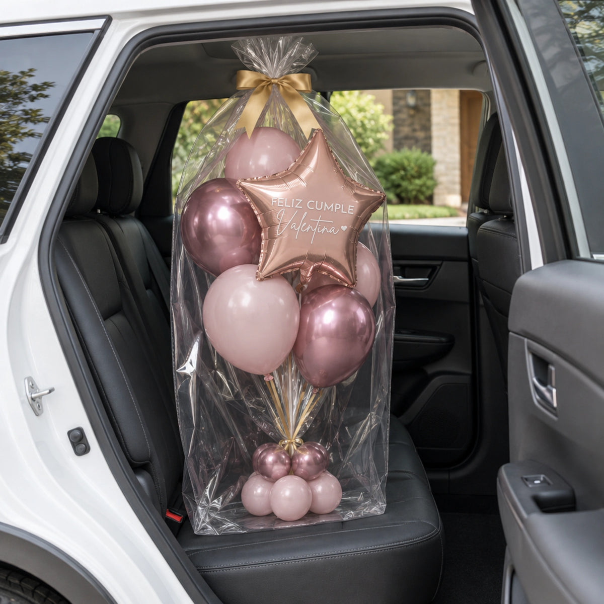 Bouquet de globos rosas con estrella, envuelto en celofán con lazo dorado en el asiento de un auto.