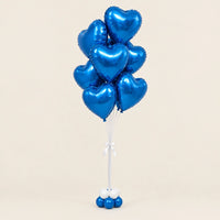 Ramo de globos de corazón azul metalizado con lazo blanco y base de globitos sobre fondo beige.