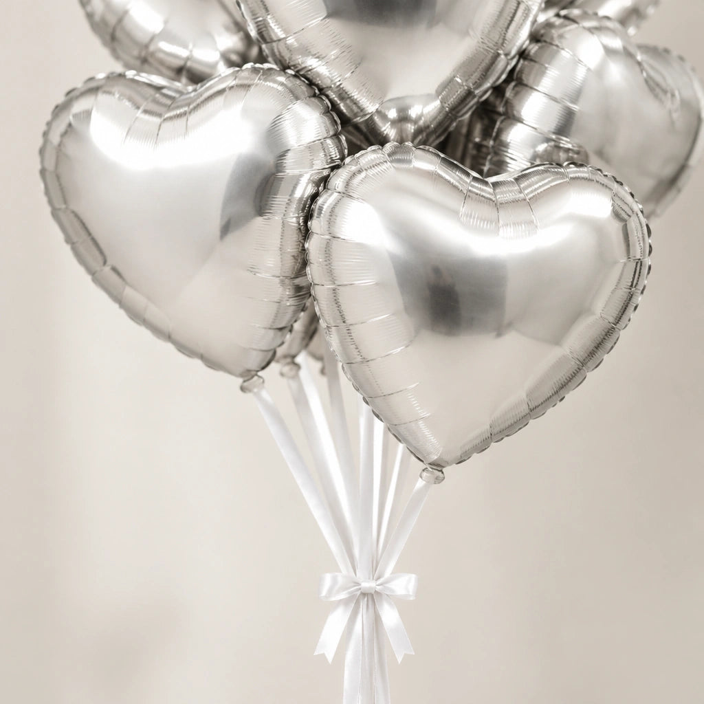 Detalle de globos de corazón plateados y cintas blancas sujetas con un lazo.