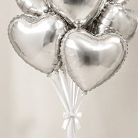Detalle de globos de corazón plateados y cintas blancas sujetas con un lazo.
