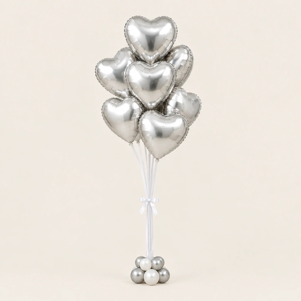 Ramo de globos de corazón plateados con lazo blanco y base de globitos, sobre fondo claro.