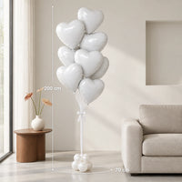 Ramo de globos de corazón blancos junto a un sofá, con medidas de 200 cm de alto y 70 cm de ancho