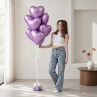 Ramo de globos de corazón lila junto a una mujer que lo sostiene y lo mira en una sala.