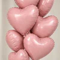 Globos de corazón rosa metalizado en primer plano, con sus brillos y costuras visibles.