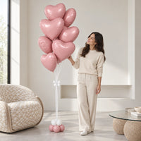 Ramo de corazones rosa en una sala, junto a una mujer que sonríe y toca un globo.