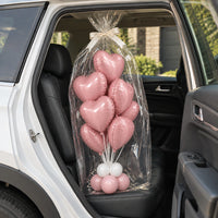 Ramo de corazones rosa envuelto en celofán con lazo blanco, sobre el asiento trasero de un auto.