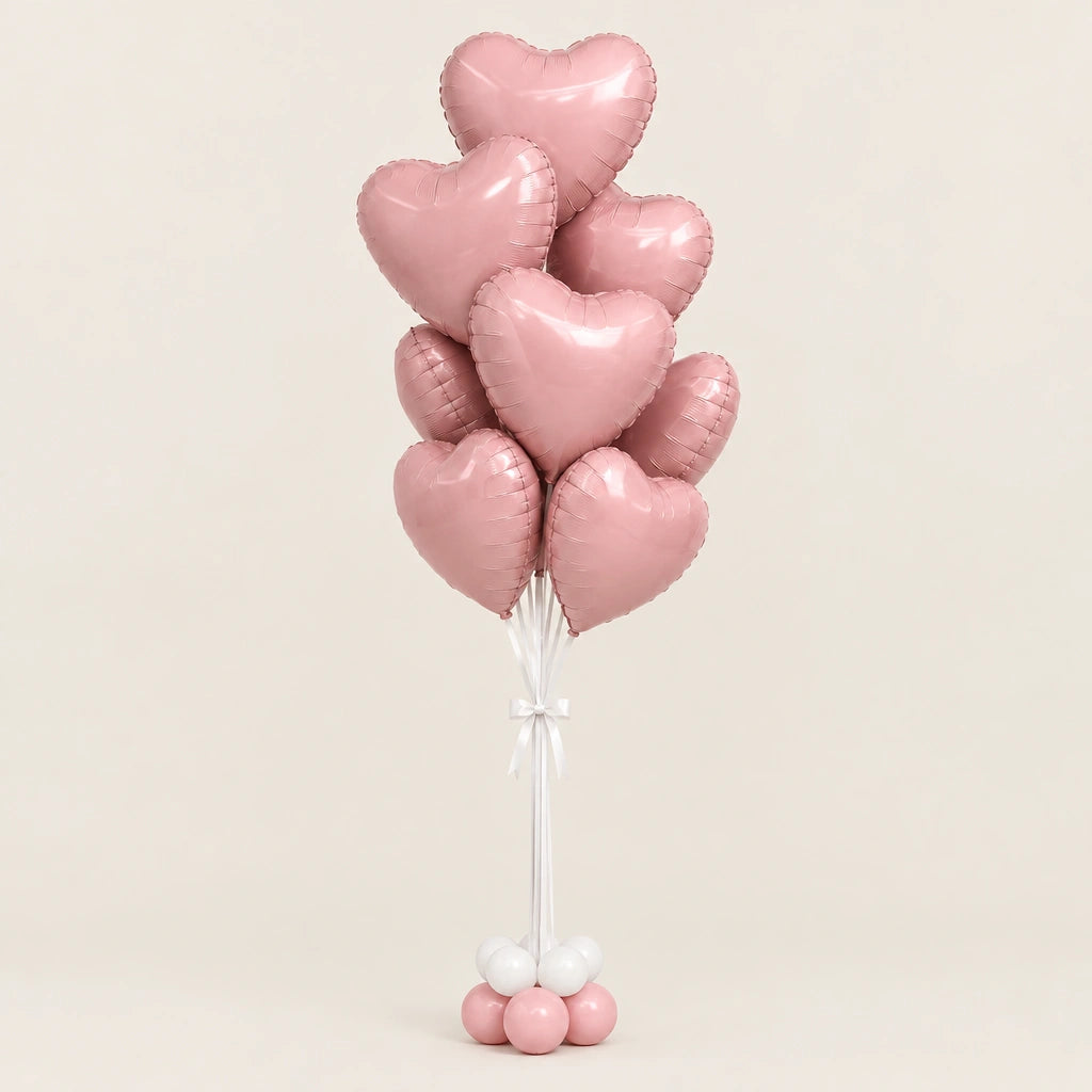 Ramo de globos de corazón rosa metalizado con lazo blanco y base de globitos, sobre fondo beige