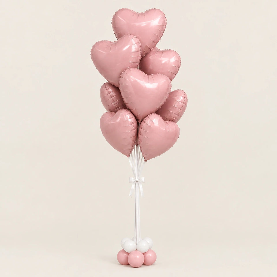 Ramo de globos de corazón rosa metalizado con lazo blanco y base de globitos, sobre fondo beige