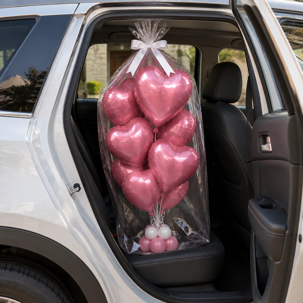 Ramo de globos de corazón rosados envuelto en celofán con lazo blanco, en el asiento trasero de un auto.