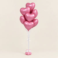Ramo de globos de corazón rosados con cintas blancas y base de globitos, sobre fondo beige.