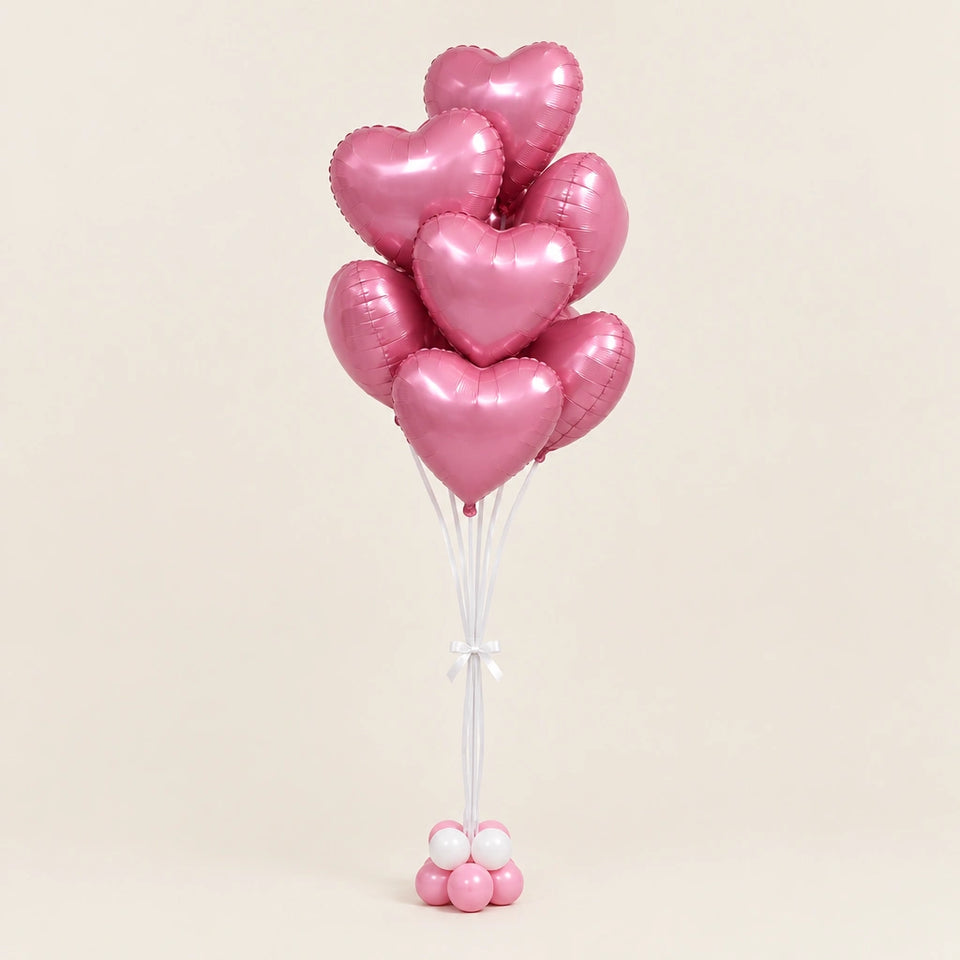 Ramo de globos de corazón rosados con cintas blancas y base de globitos, sobre fondo beige.